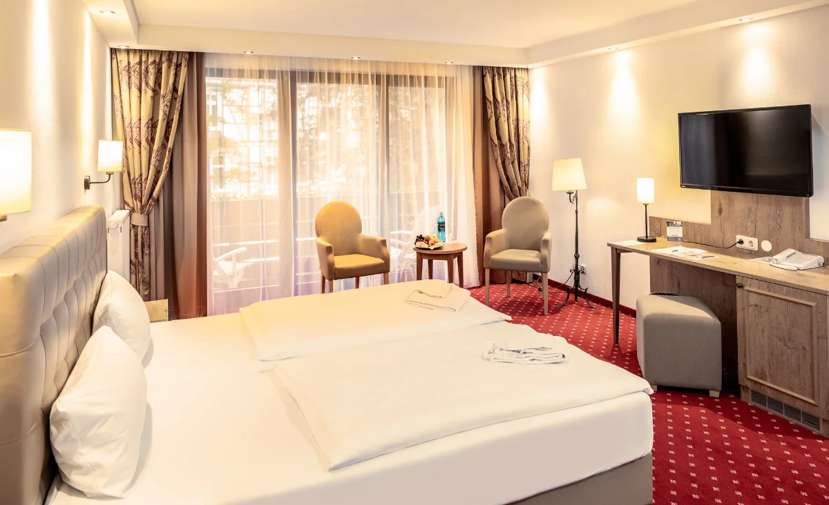 Hotelzimmer im Mühl Vital Resort: Bett, Schreibtisch, Stuhl, Fernseher und Fenster mit Blick auf die Umgebung.