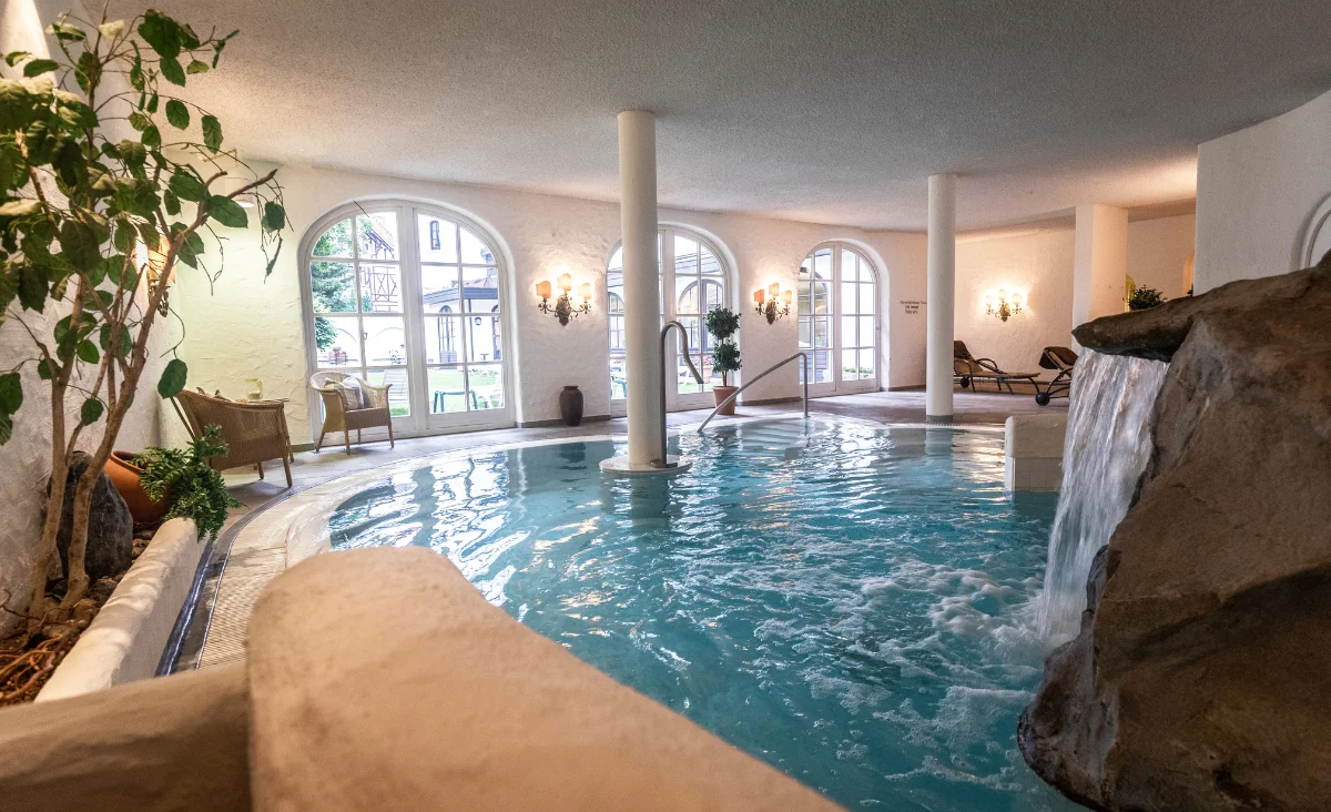 Großes Hallenbad im Mühl Vital Resort in Bad Lauterberg, mit einem beeindruckenden Wasserfall im Hintergrund.
