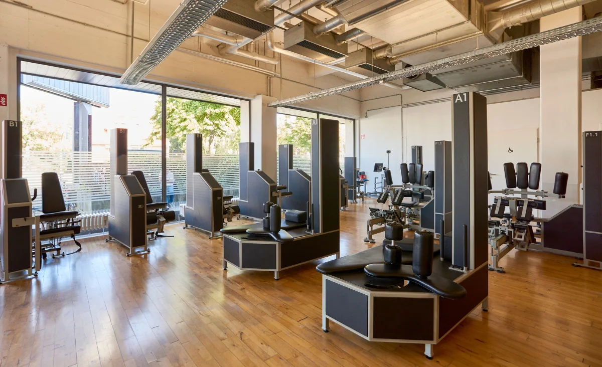 Innenraum eines Kieser Training Studios Berlin mit mehreren Krafttrainingsgeräten auf Holzboden und großen Fenstern