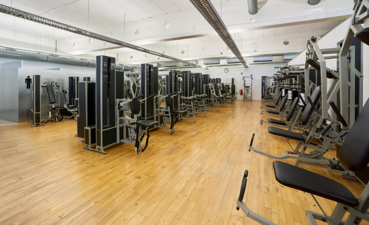 Innenraum eines Kieser Training Studios Berlin mit mehreren Krafttrainingsgeräten auf Holzboden und großen Fenstern