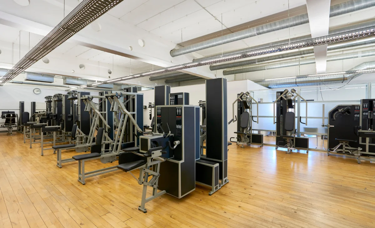 Innenraum eines Kieser Training Studios Berlin mit mehreren Krafttrainingsgeräten auf Holzboden und großen Fenstern