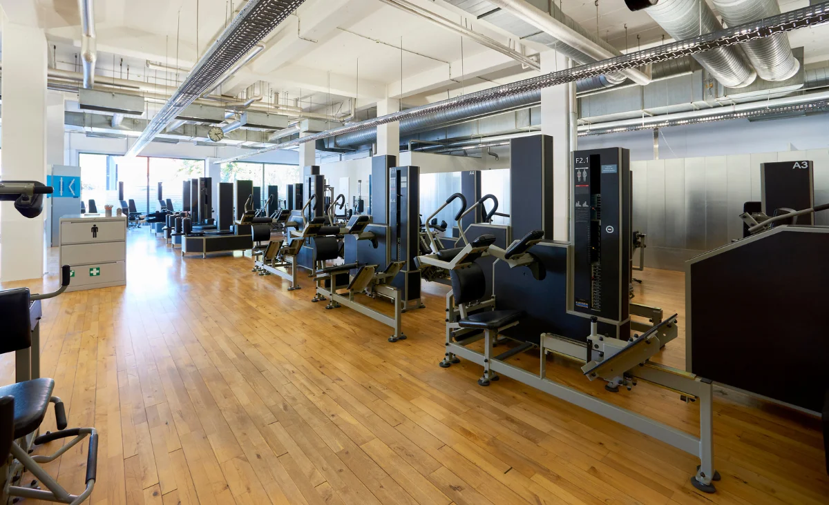 Innenraum eines Kieser Training Studios Berlin mit mehreren Krafttrainingsgeräten auf Holzboden und großen Fenstern