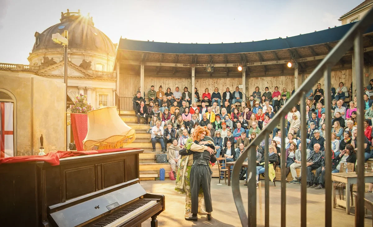 Bühnenaufnahme im Monbijou Theater Berlin mit zwei Schauspielern in der Bühnenmitte und Publikum auf den Rängen im Hintergrund