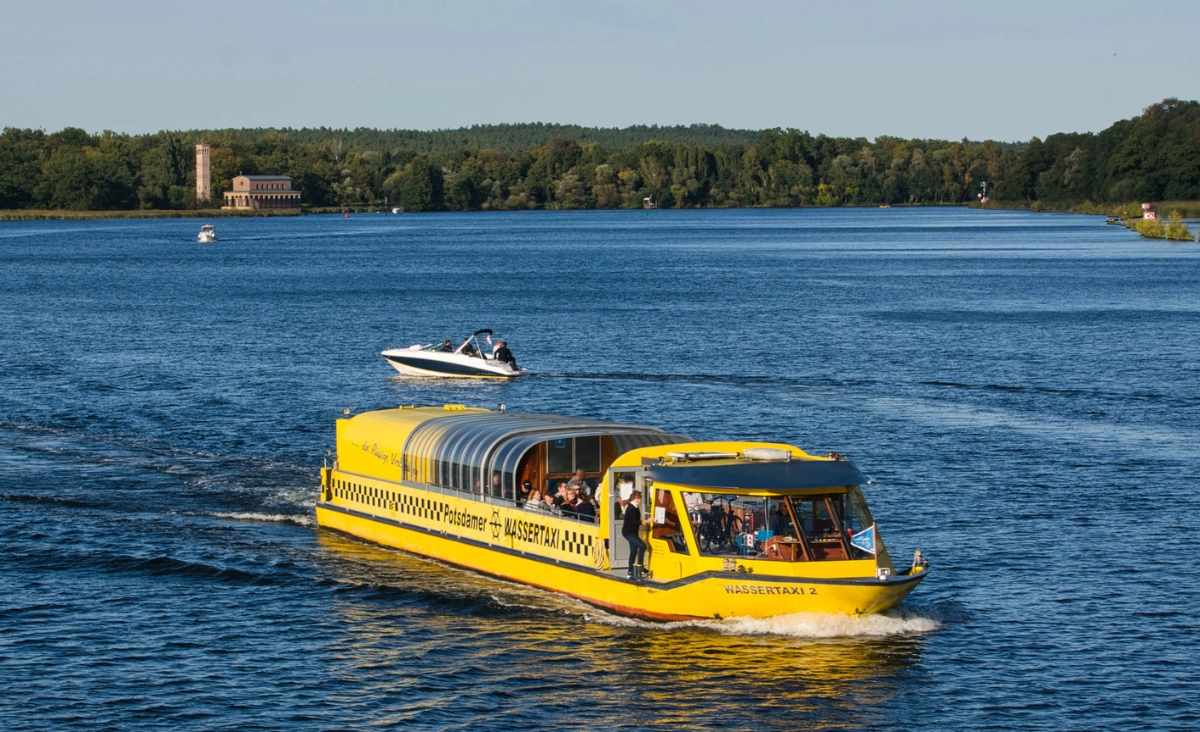 Ein Wassertaxi fährt auf dem Wasser in Potsdam, umgeben von malerischer Landschaft.