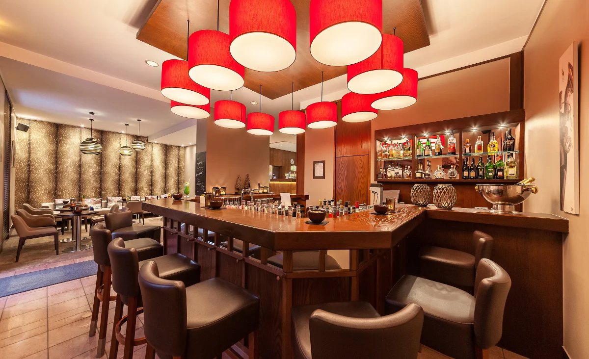 Barbereich mit hölzernem Tresen, mehreren Barhockern und großen, runden Deckenlampen in einem Wellnesshotel in Bad Steben