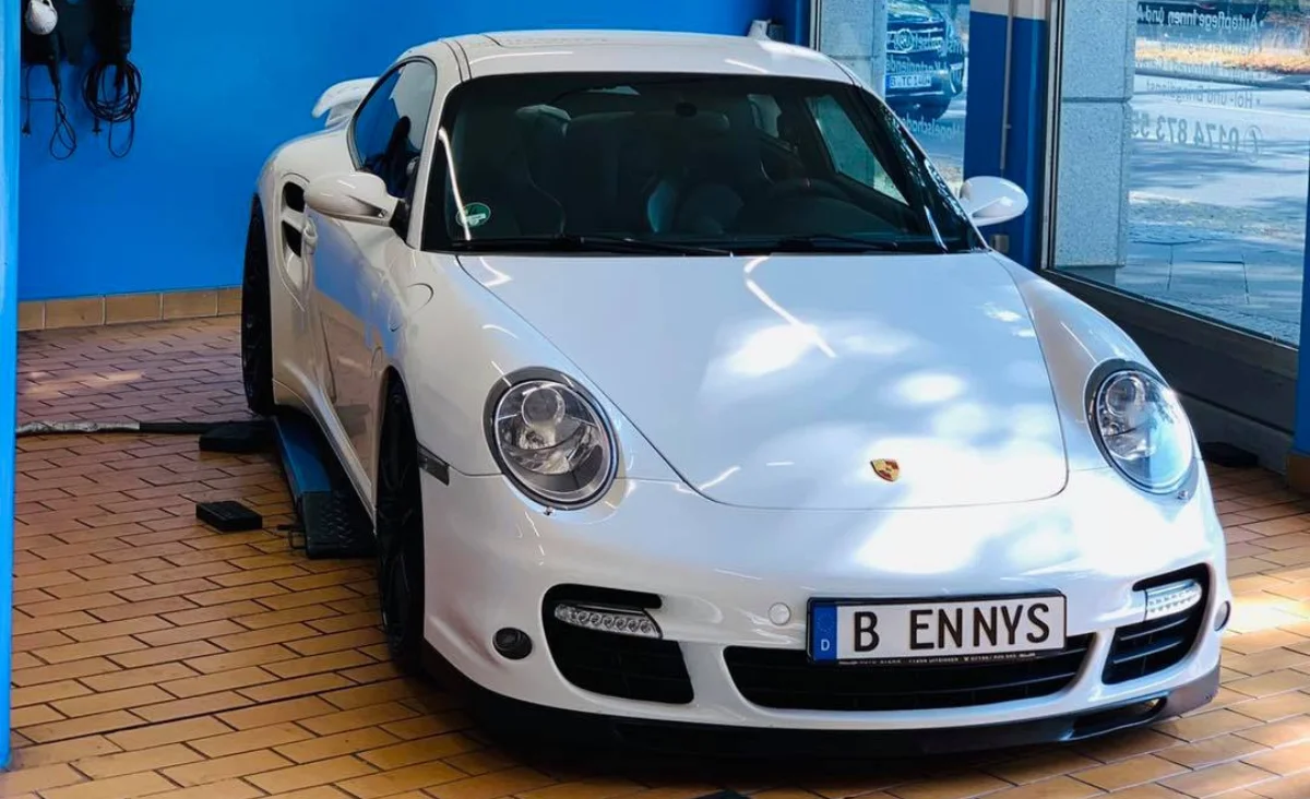 Weiße Porsche-Sportwagen-Front mit runden Scheinwerfern und Berliner Kennzeichen 'B ENNYS' in einer Autopflegewerkstatt mit blauem Hintergrund