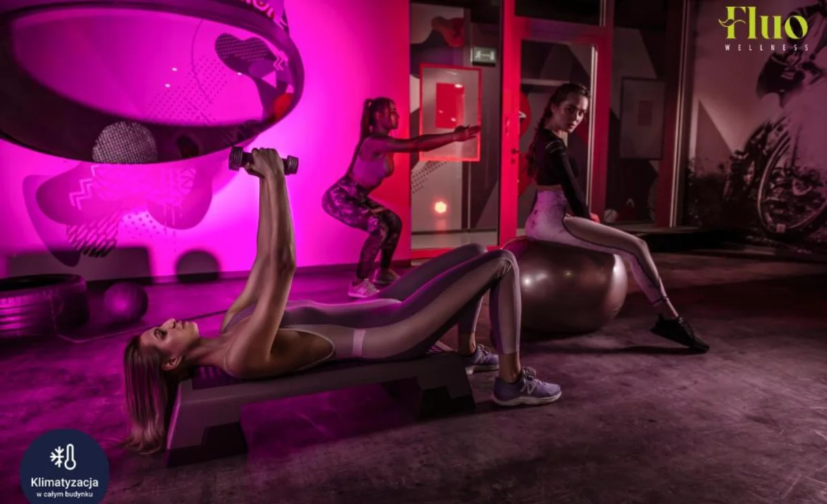Im Grape Town Hotel in Zielona Góra nutzen Frauen Fitnessgeräte in einem pink beleuchteten Fitnessbereich.