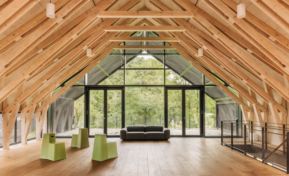 Großer, offener Raum mit sichtbarer Holzkonstruktion, bodentiefen Fenstern und moderner Sitzgruppe mit grünlichen Stühlen und schwarzem Sofa im Astraea Eco Resort