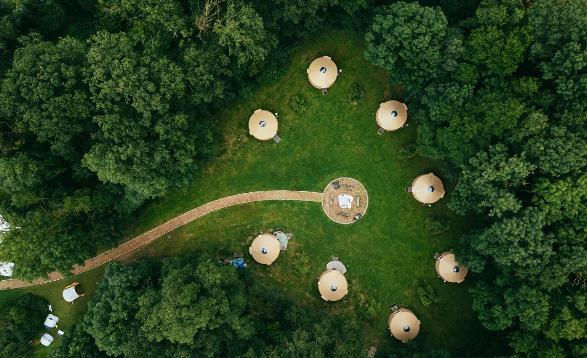 Luftaufnahme des Astraea Eco Resort mit mehreren runden Zelten auf einer grünen Wiese, umgeben von dichtem Wald und einem geschwungenen Weg