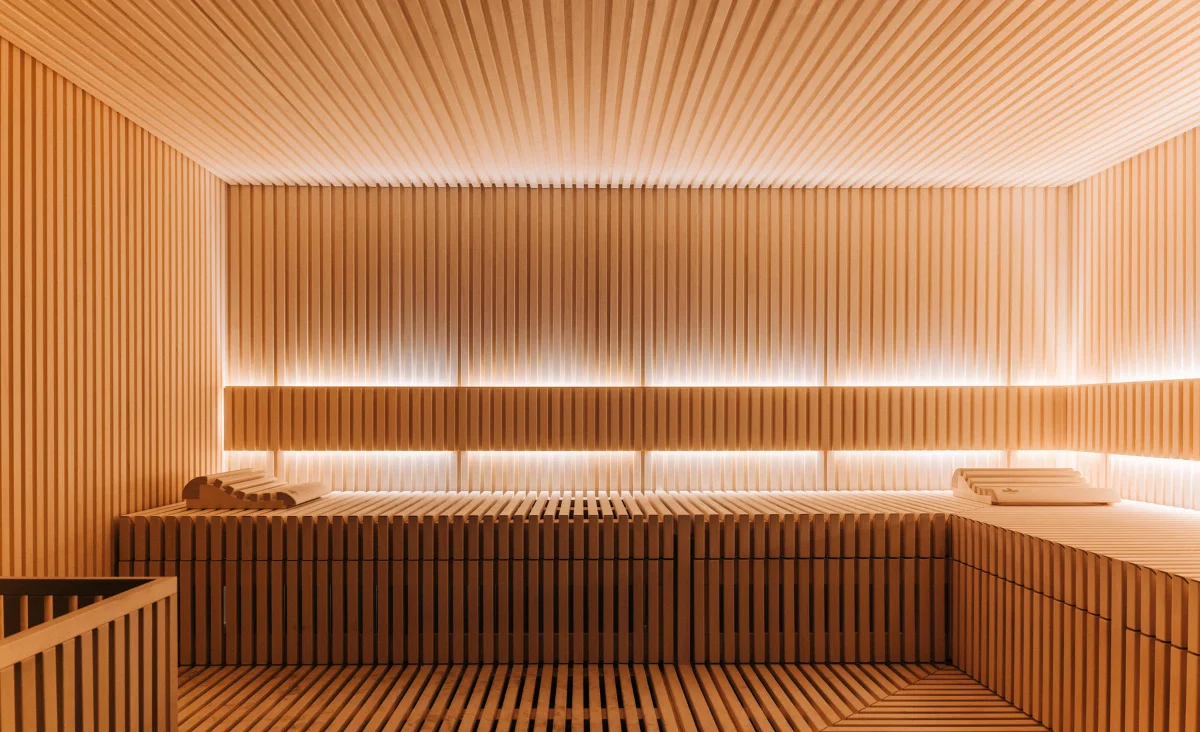 Innenraum einer Sauna mit hellen Holzlatten an Wänden, Decke und Sitzbänken sowie indirekter Beleuchtung