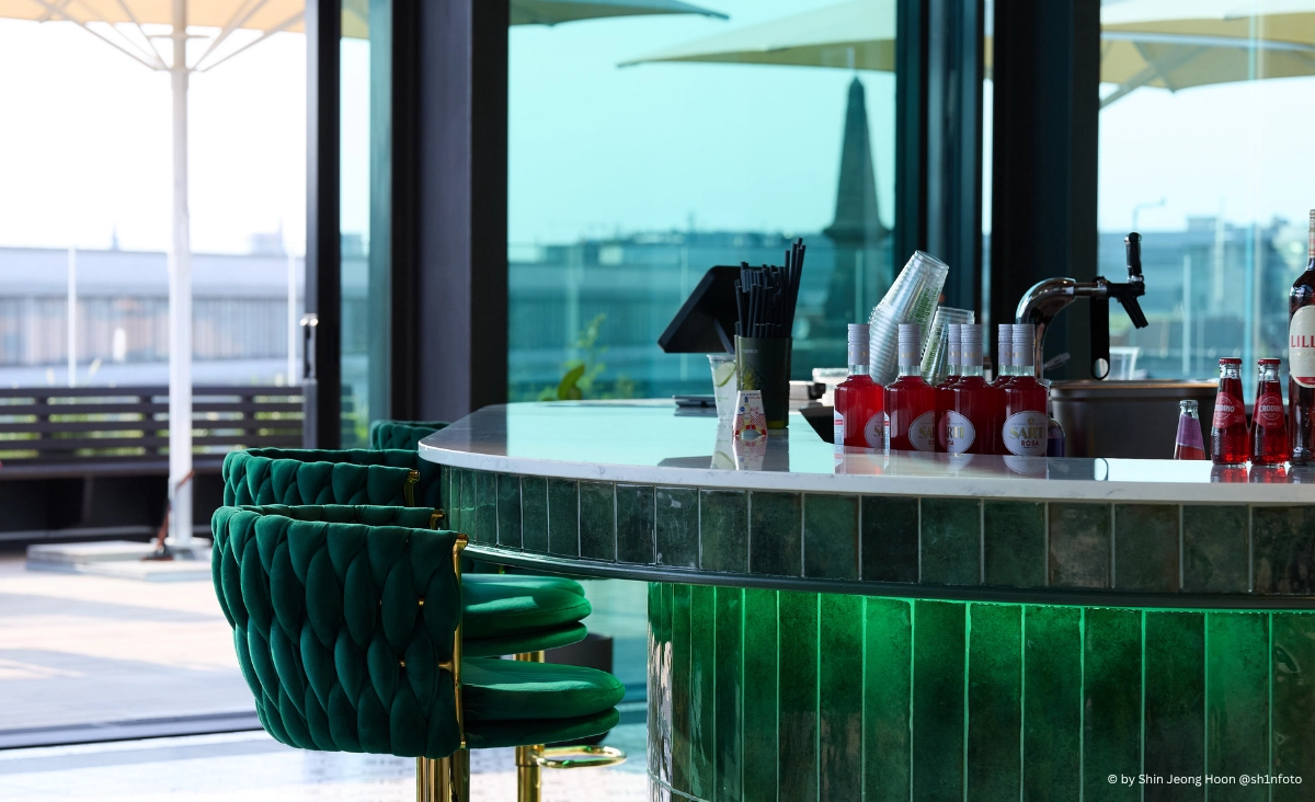 Gemütliche Bar des "The Dawn Berlin" mit grünen Stühlen und einer stilvollen Theke, ideal für gesellige Abende.