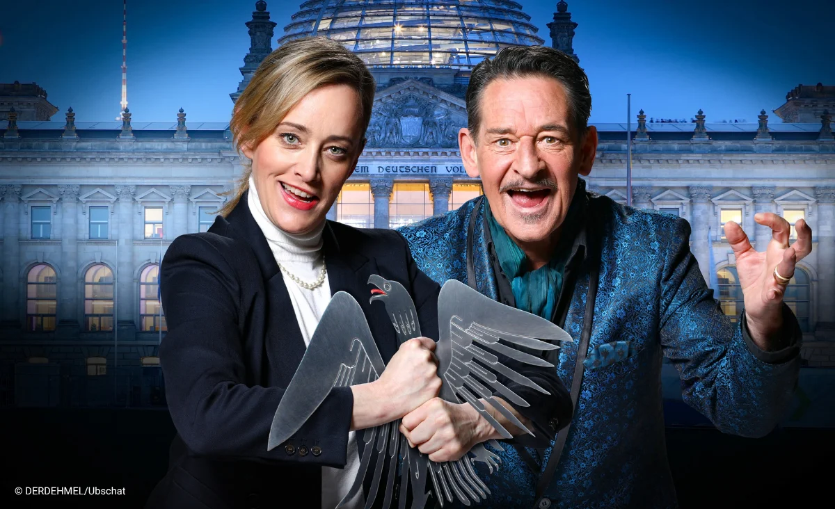 Zwei Schauspieler vor dem Reichstagsgebäude, die eine stilisierte schwarze Adlerfigur halten. Putsch Theaterstück im Schlosspartk Theater