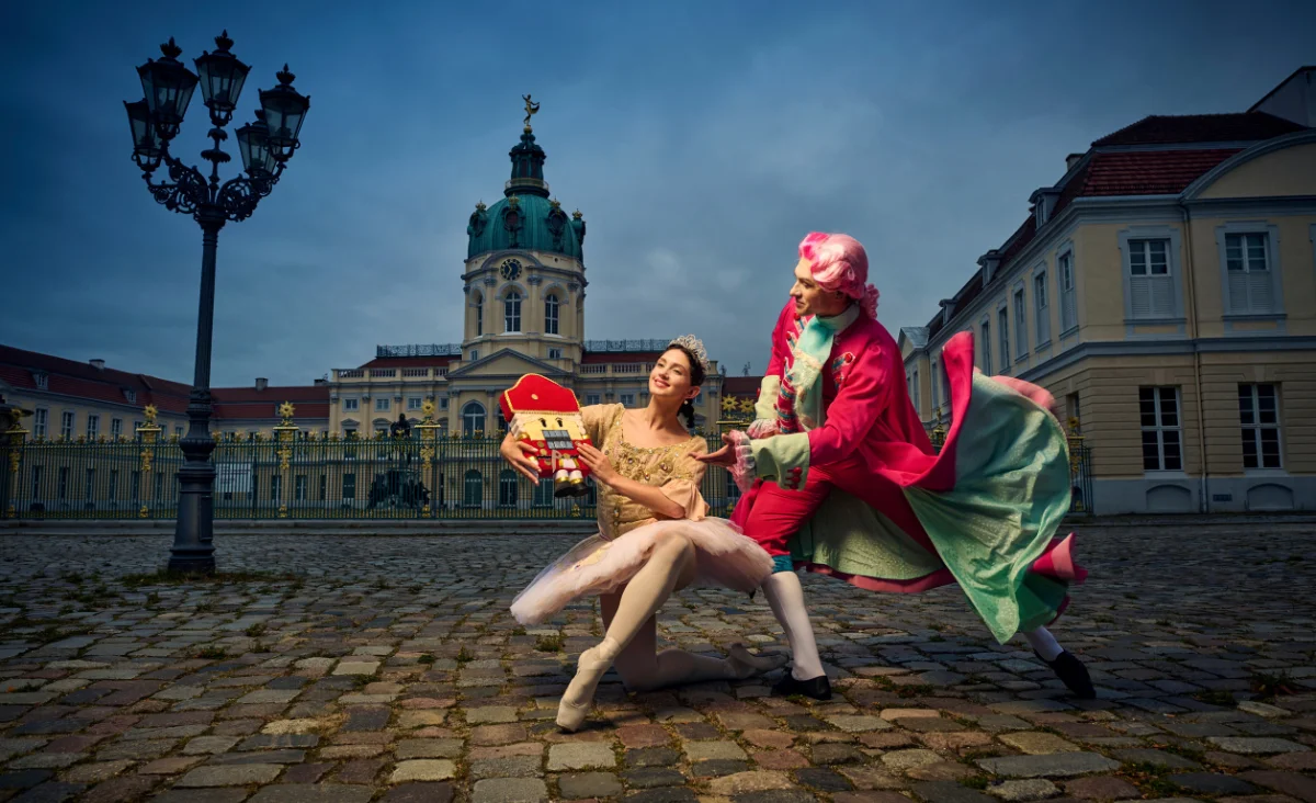 Zwei Balletttänzer in historischen Kostümen posieren vor dem Schloss Charlottenburg, die Frau hält eine Nussknacker-Figur